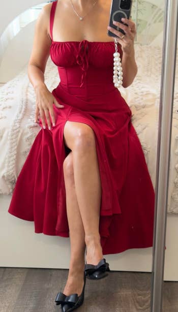 Woman successful a stylish sleeveless dress, taking a reflector selfie. She is sitting connected a bed, wearing a classical brace of achromatic shoes