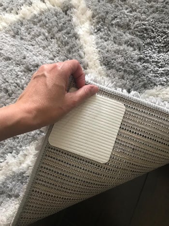 a reviewer shows the grip attached to their gray rug