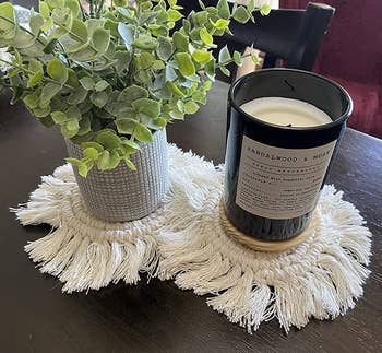 a plant and a candle sitting on two macrame coasters