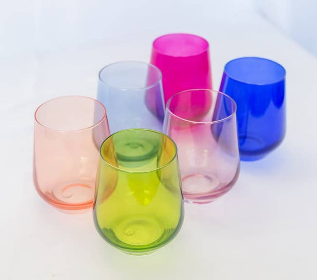 Five variously shaped, colorful drinking glasses on a white surface, ideal for modern table settings