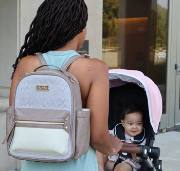 mother wearing taupe mini backpack, pushing stroller