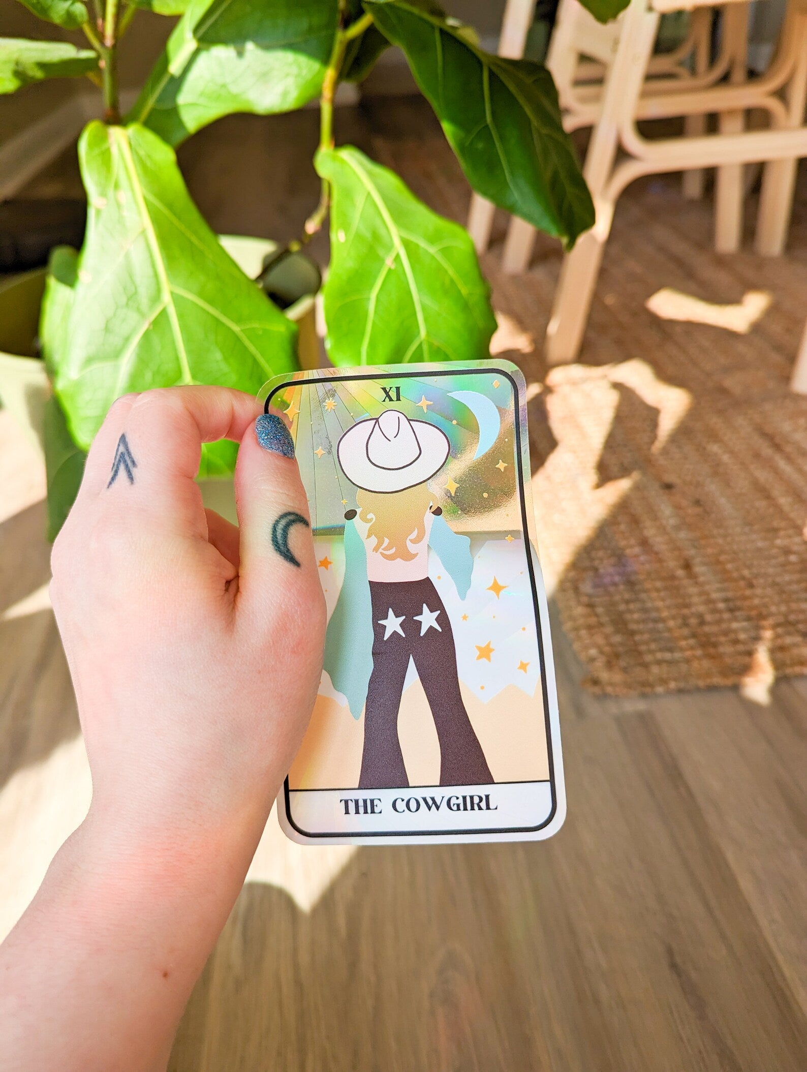 A tarot card style window catcher with a blonde cowgirl facing away wearing a white cowboy hat and jeans with stars on the back pockets 