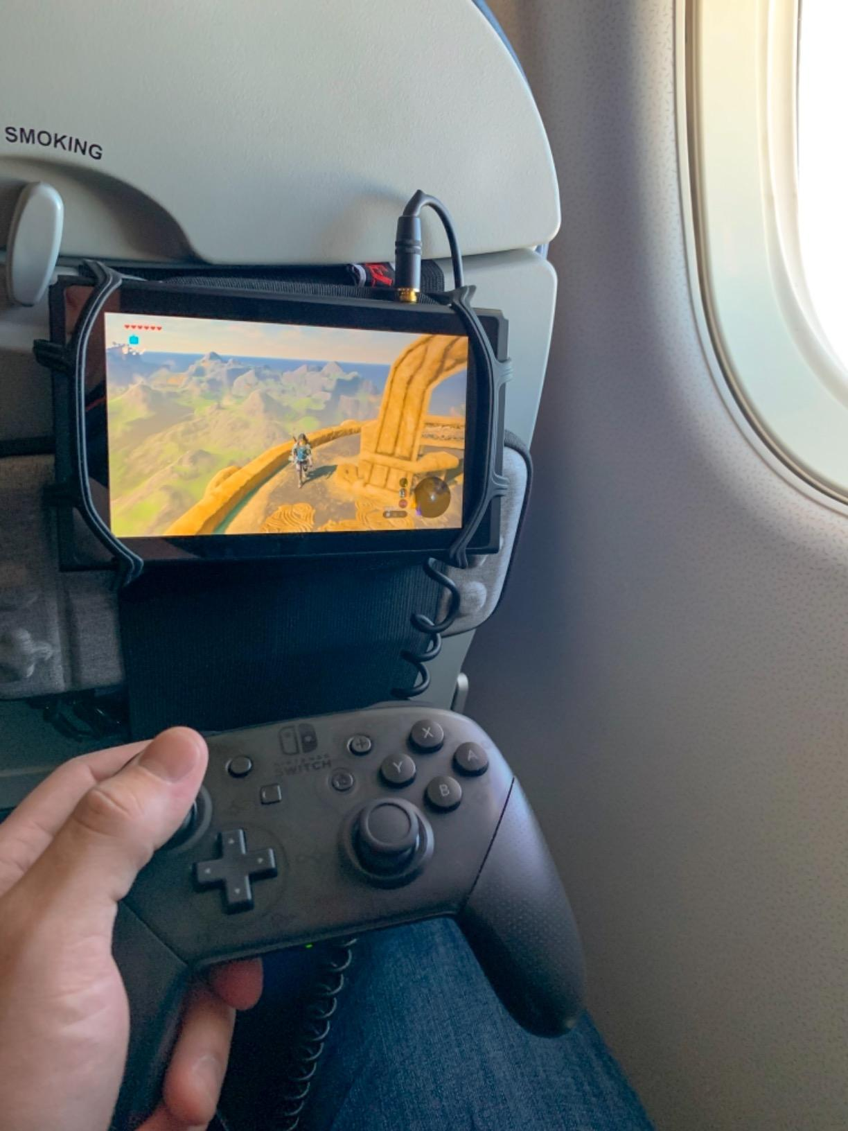 A idiosyncratic   plays a video crippled  connected  a handheld console mounted to an airplane seat, holding a wireless controller
