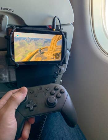 A idiosyncratic plays a video crippled connected a handheld console mounted to an airplane seat, holding a wireless controller
