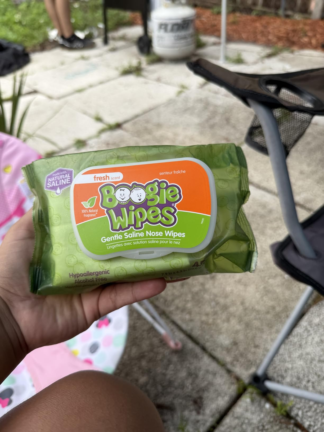 Person holding a battalion  of Boogie Wipes, gentle saline chemoreceptor  wipes, outdoors with chairs and factual  patio visible