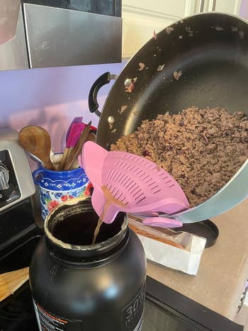 Ground nutrient   is being strained with a pinkish  strainer from a frying pan