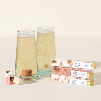 Two glasses of sparkling wine beside four boxes of marshmallows with luxury branding, suggesting elegant confectionery