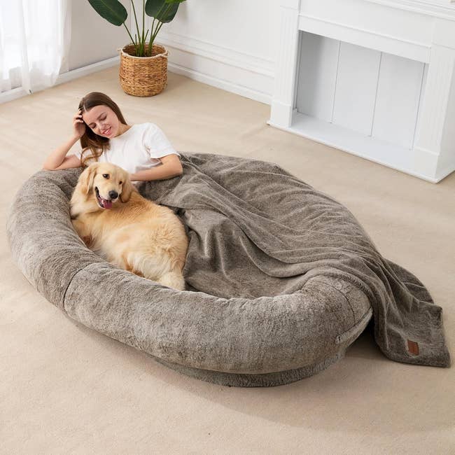 Model lying with dog in a brown oval rimmed bed on the floor