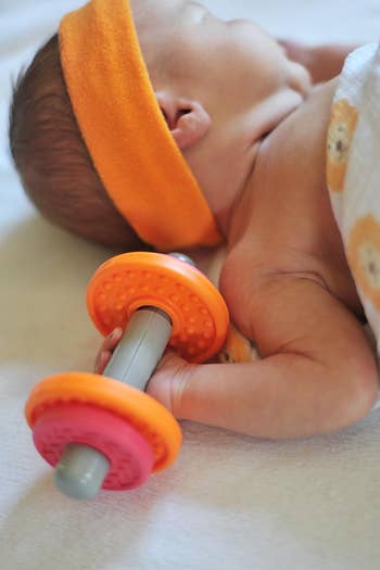 Infant laying down with a silicone baby toy shaped like a dumbbell
