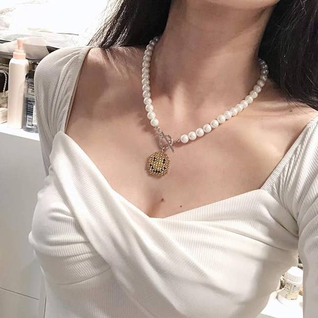 Close-up of a model wearing a pearl necklace with a prominent pendant, posing in a white off-shoulder top
