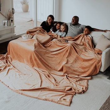 two adult models and three kid models under the large tan blanket