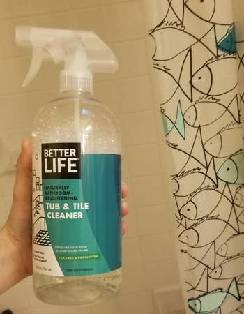 Hand holding a bottle of Better Life bathroom cleaner against a shower curtain backdrop