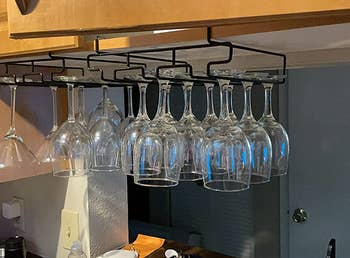 reviewer using two of the black three row racks to hang glasses under a cabinet