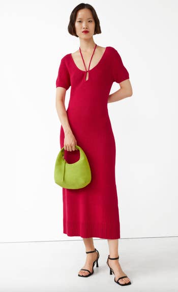 model wearing red knit midi dress, holding green bag