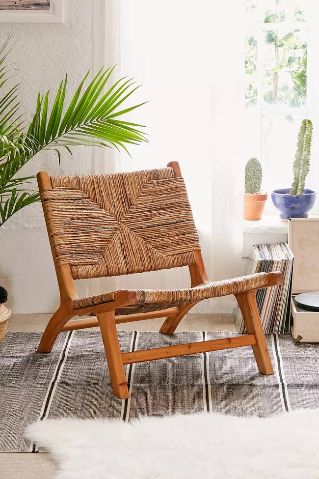 Woven lounge chair on a striped rug, set next to a sunny window with plants and vinyl records, showcasing a cozy boho style