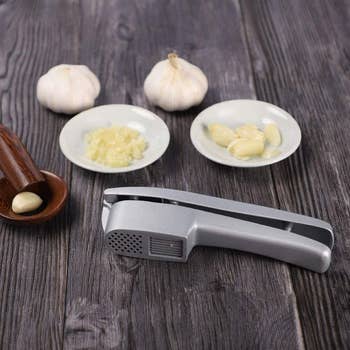 the silver garlic press next to bowls holding both minced and sliced garlic
