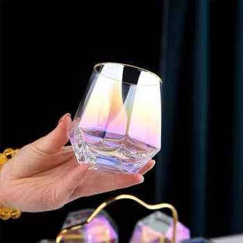 Hand holding a clear, iridescent whiskey glass, suitable for elegant table settings