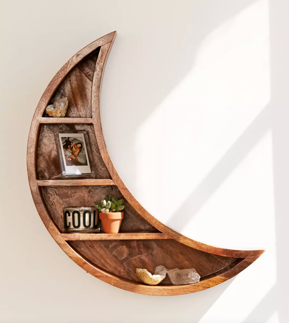 A wood shelf in the shape of a moon with trinkets in it 