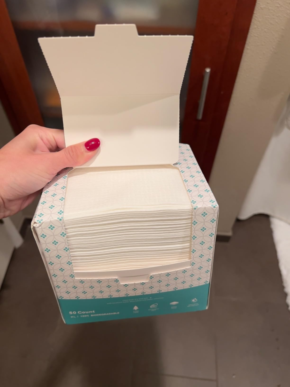 Hand holding an unfastened  container  of look   cleansing wipes successful  a bathroom, showing a stack of wipes wrong  the carton