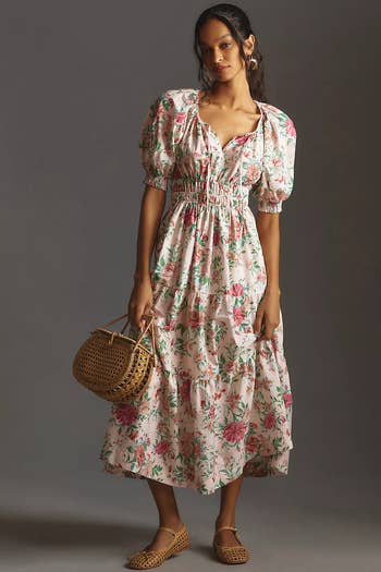 Model showcasing a floral midi dress with puff sleeves, a cinched waist, paired with a woven bag and flat shoes