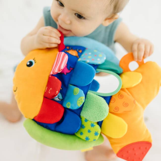Child playing with a colorful plush food  artifact  with assorted  textures and patterns, promoting sensory play