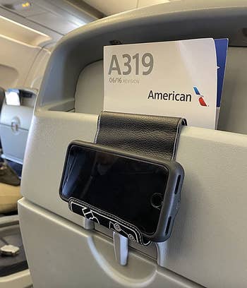 A black foldable holder hung on an airplane seat with a phone in it 