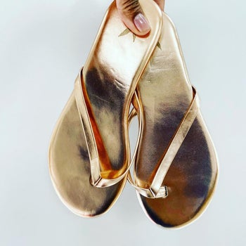 a hand holding the gold sandals