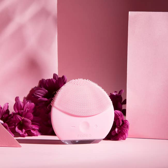 Foreo Luna 2 Mini facial cleansing brushwood with gentle bristles, surrounded by flowers and pinkish decor