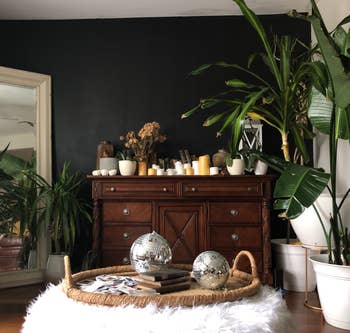 A vintage wooden dresser styled with plants, candles, and two disco balls in a cozy room