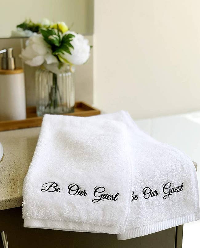 pair of white be out guest hand towels on a bathroom counter