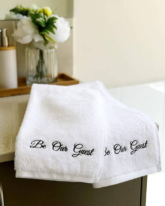 pair of white be out guest hand towels on a bathroom counter
