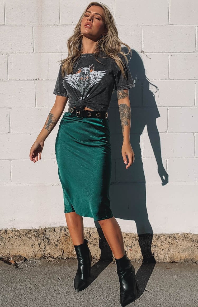 Model is wearing a charcoal grey top and an emerald green midi skirt