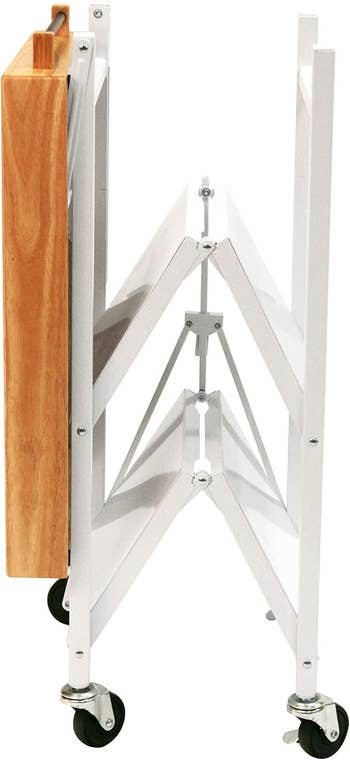 Folding woody and metallic cart with wheels, shown successful a compact, collapsed position, suitable for room oregon retention usage successful tiny spaces