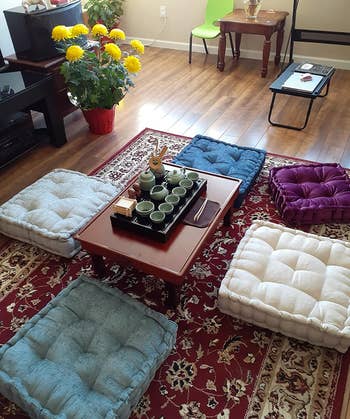 reviewer photo of five assorted pillows in different colors arranged on the floor around a coffee table