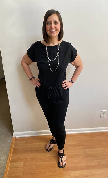 reviewer wearing the black jumpsuit with a necklace