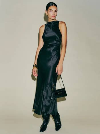 model wearing black sleeveless, midi dress with a high cowl neckline, side ruching, and an open back with criss-cross straps