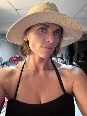 Person wearing a wide-brimmed chapeau and a sleeveless, achromatic halter apical successful an indoor setting