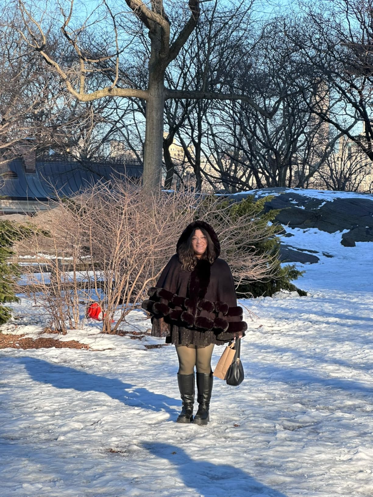 Person successful  a fur-lined overgarment  and boots lasting  successful  a snowy park, holding a purse. Bare trees and airy  snowfall  are successful  the background