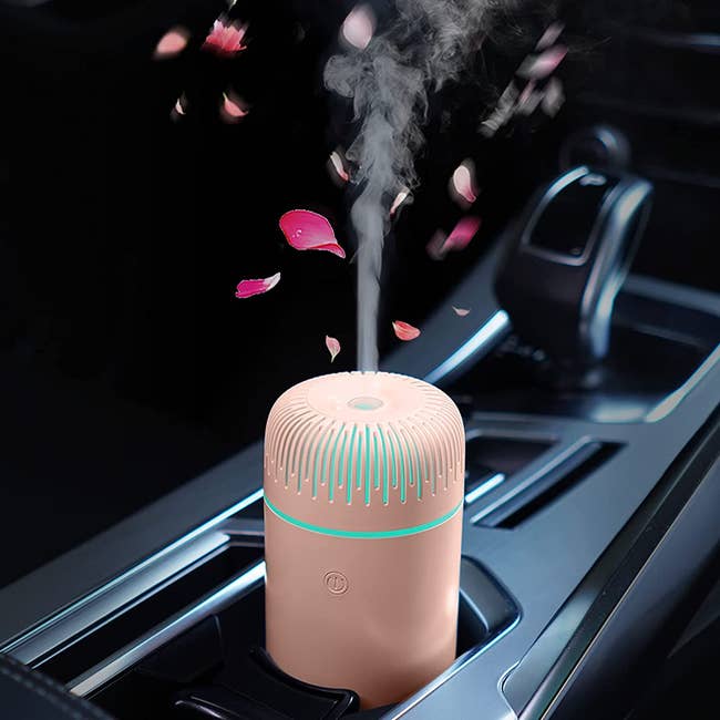 The pink cylinder shaped diffuser releasing air into a car from the drink holder 