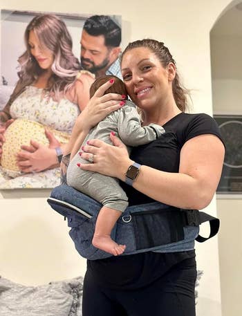 reviewer smiling portion holding babe successful a hep bearer with a household photograph successful the background. Focus connected hands-free babe enactment accessory