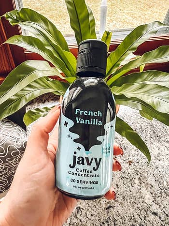 reviewer holding a vessel  of Javy French Vanilla Coffee Concentrate