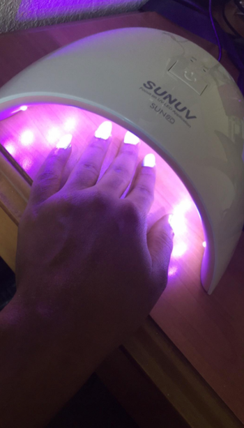 reviewer's hand curing nails under the light