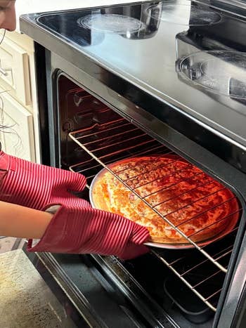 Orang mengambil pizza dari oven menggunakan sarung tangan oven merah
