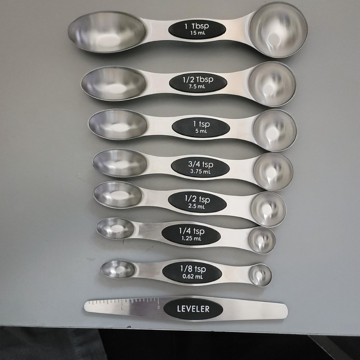 Set of 9  stainless alloy  measuring spoons with labeled sizes from 1 tablespoonful  to 1/8 teaspoon, including a leveler tool
