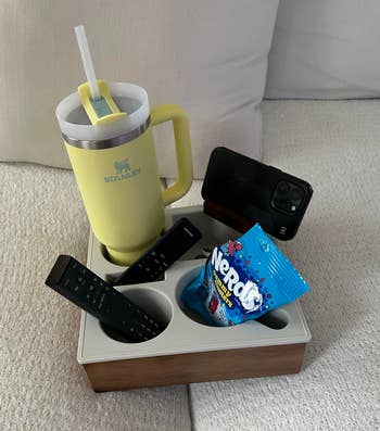 Organizing tray holds a Stanley tumbler, phone, 2 remotes, and a candy bag, perfect for sofa-side convenience