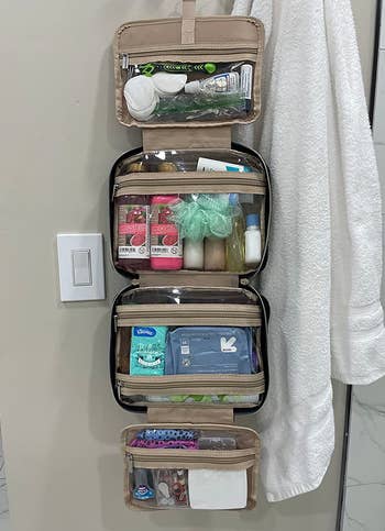 reviewer photo of the unfolded toiletry bag filled with products hanging on a bathroom wall
