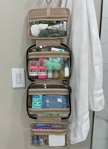 reviewer photo of the unfolded toiletry bag filled with products hanging on a bathroom wall