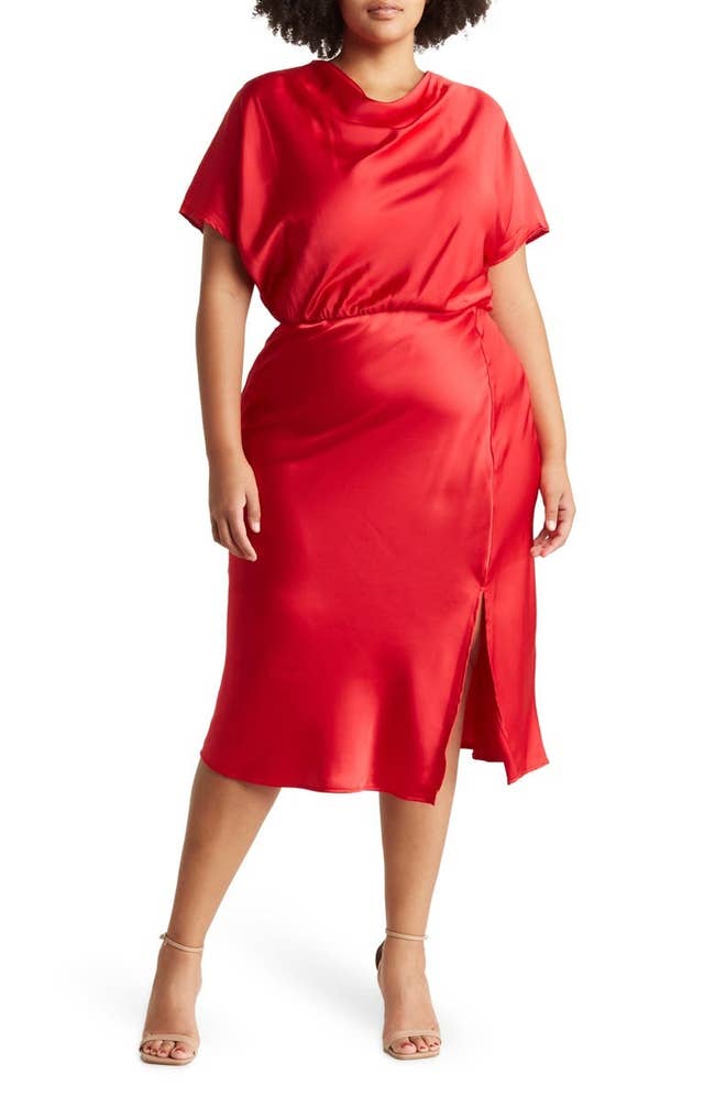 Person in a sleek, short-sleeve, satin dress with a side slit, styled with neutral strappy heels, standing in a fashion-forward pose