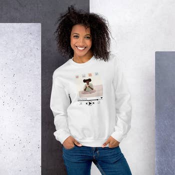 a model in a white crewneck with a graphic of a girl sitting cross legged with tea and a 