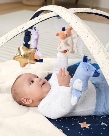 Baby lying connected  a play   mat, reaching for hanging plush toys shaped similar  animals and a star, suitable for a buying  context